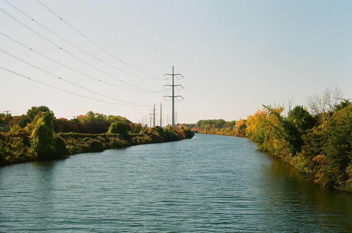 An analog photo scan of a river in autumn, bordered by trees and power lines.